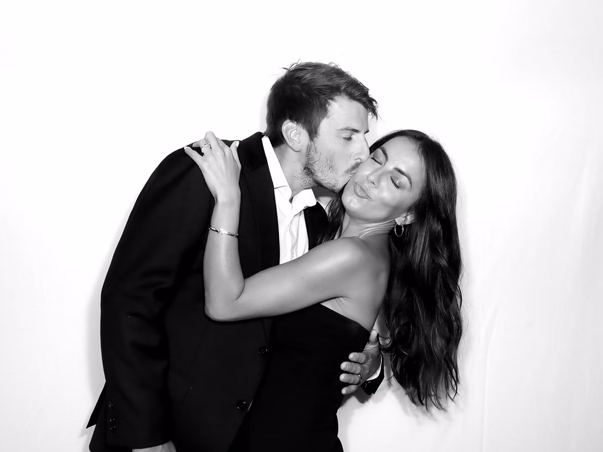 A couple kissing on the cheek at a wedding with an Infinite Magic Photo Booth Rental